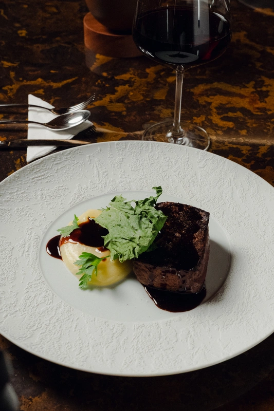 Prato da gastronomia premium servido na Sala VIP Pedra Preta do Itaú Personnalité em Guarulhos, acompanhado de vinho em ambiente sofisticado.
