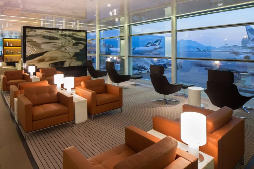 Sala VIP de aeroporto com poltronas de couro, iluminação aconchegante, janelas panorâmicas e vista para aviões estacionados no terminal.